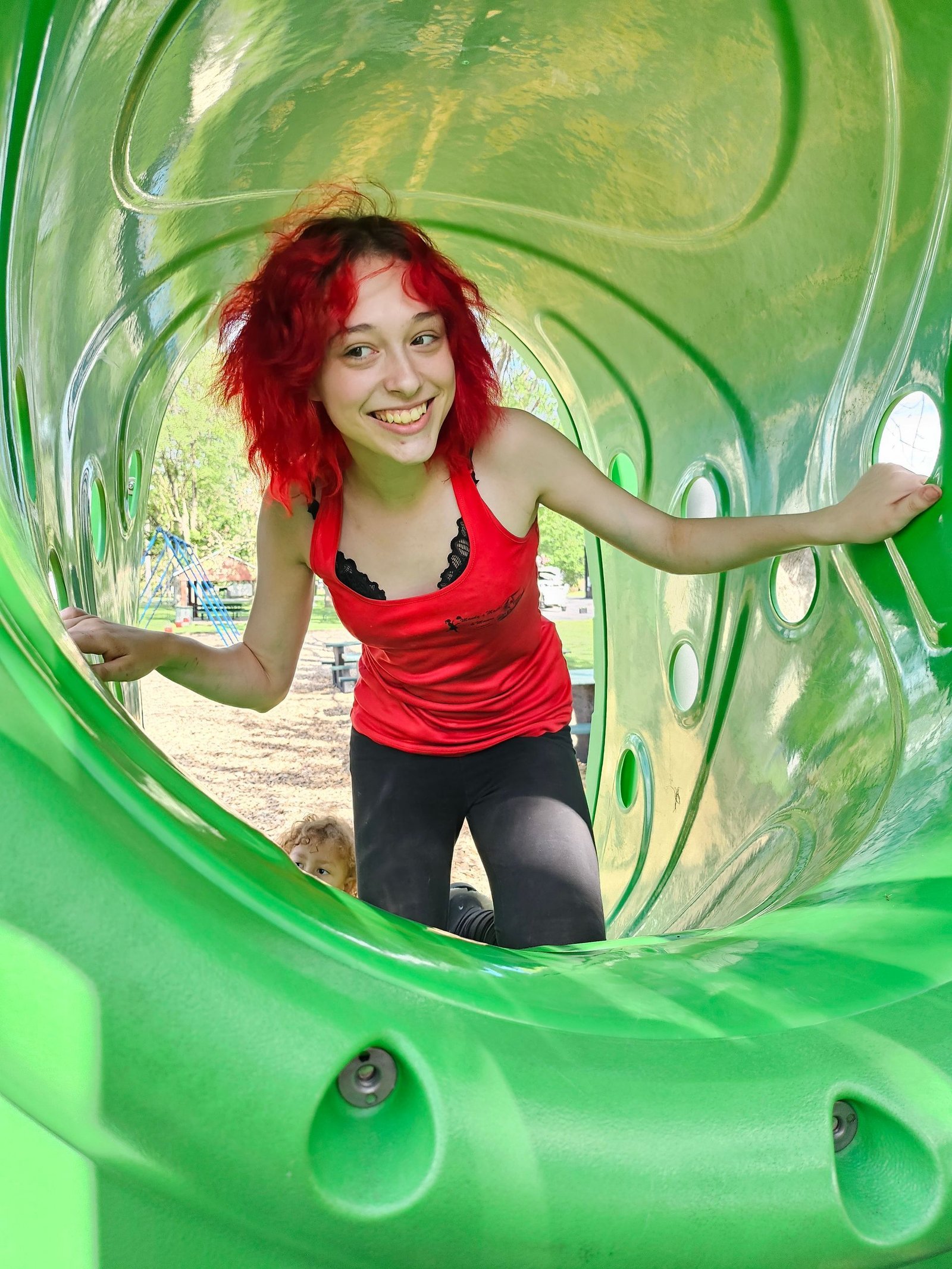A girl with red hair is playing in a green tunnel.