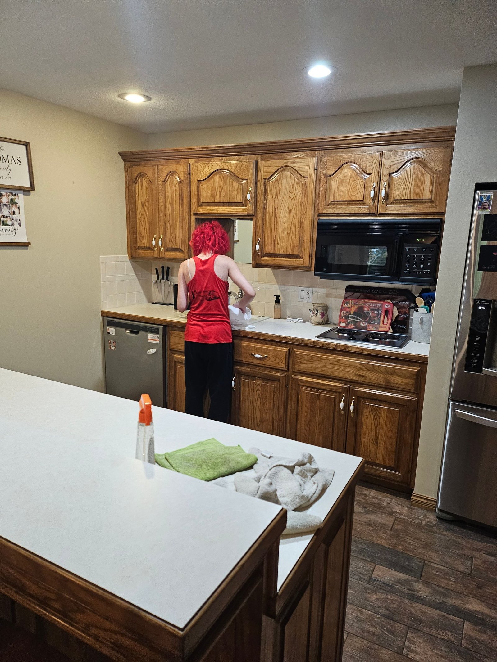 A woman in a red tank top is standing in a kitchen.