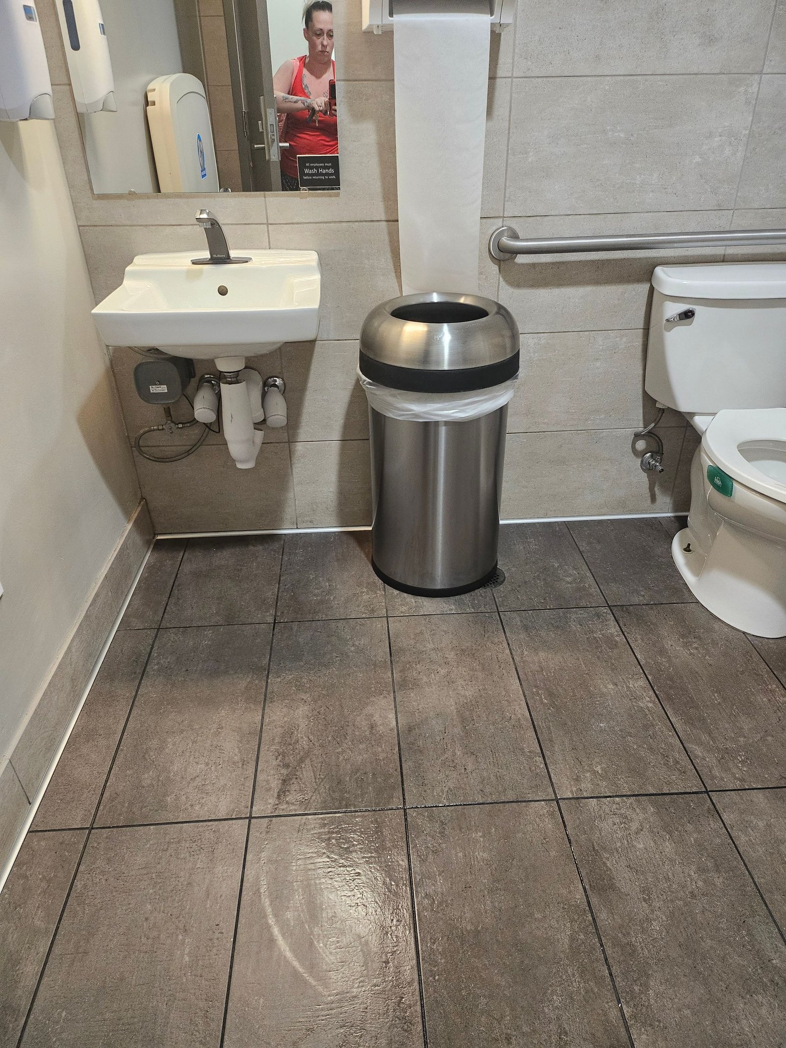 A bathroom with a sink, toilet, trash can and mirror.